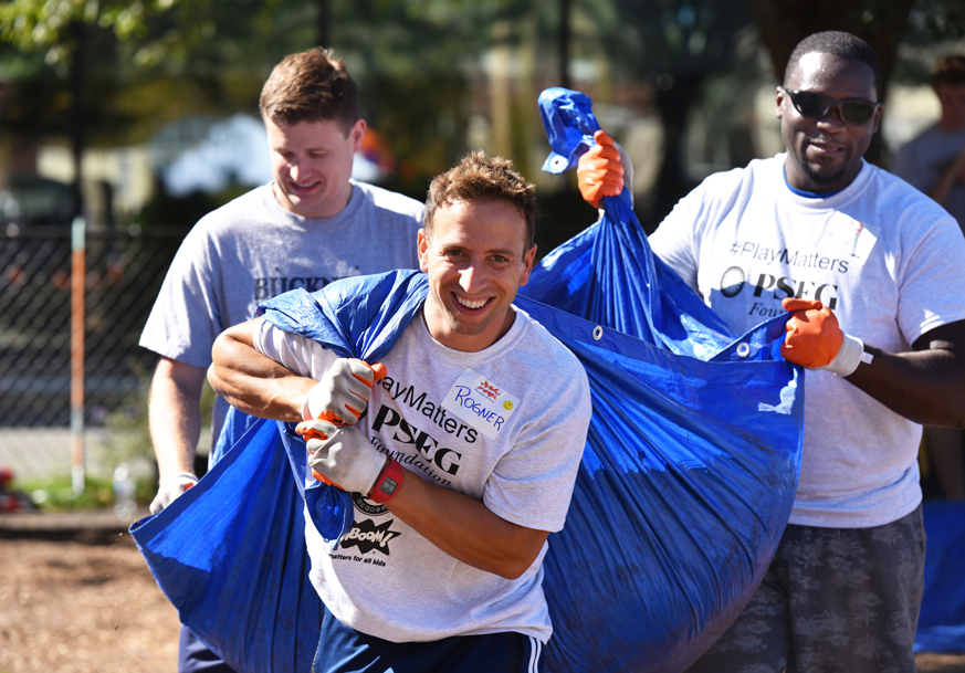 PSEG employee volunteers carrying a tarp filled with leaves