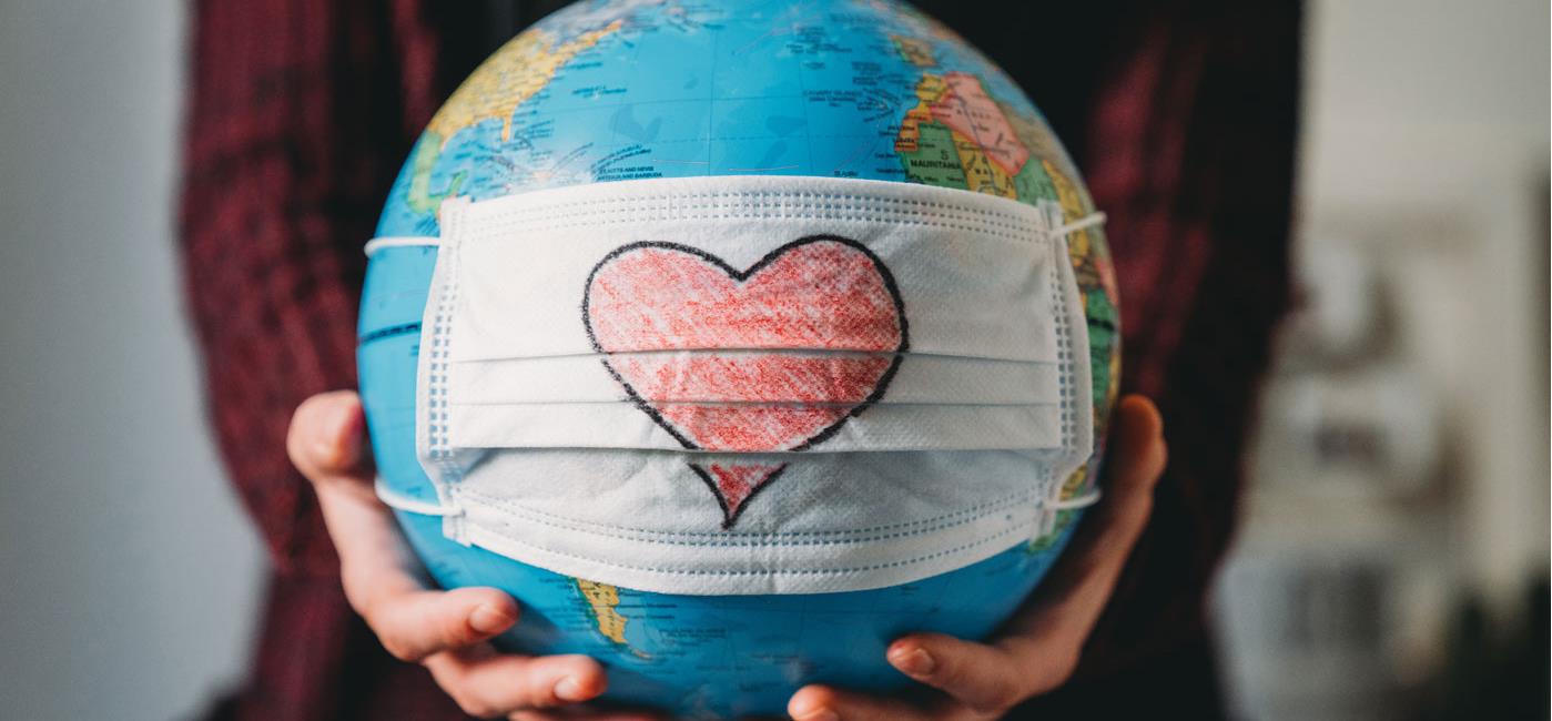 Person holding a globe of the earth with a mask and heart pictured on it.